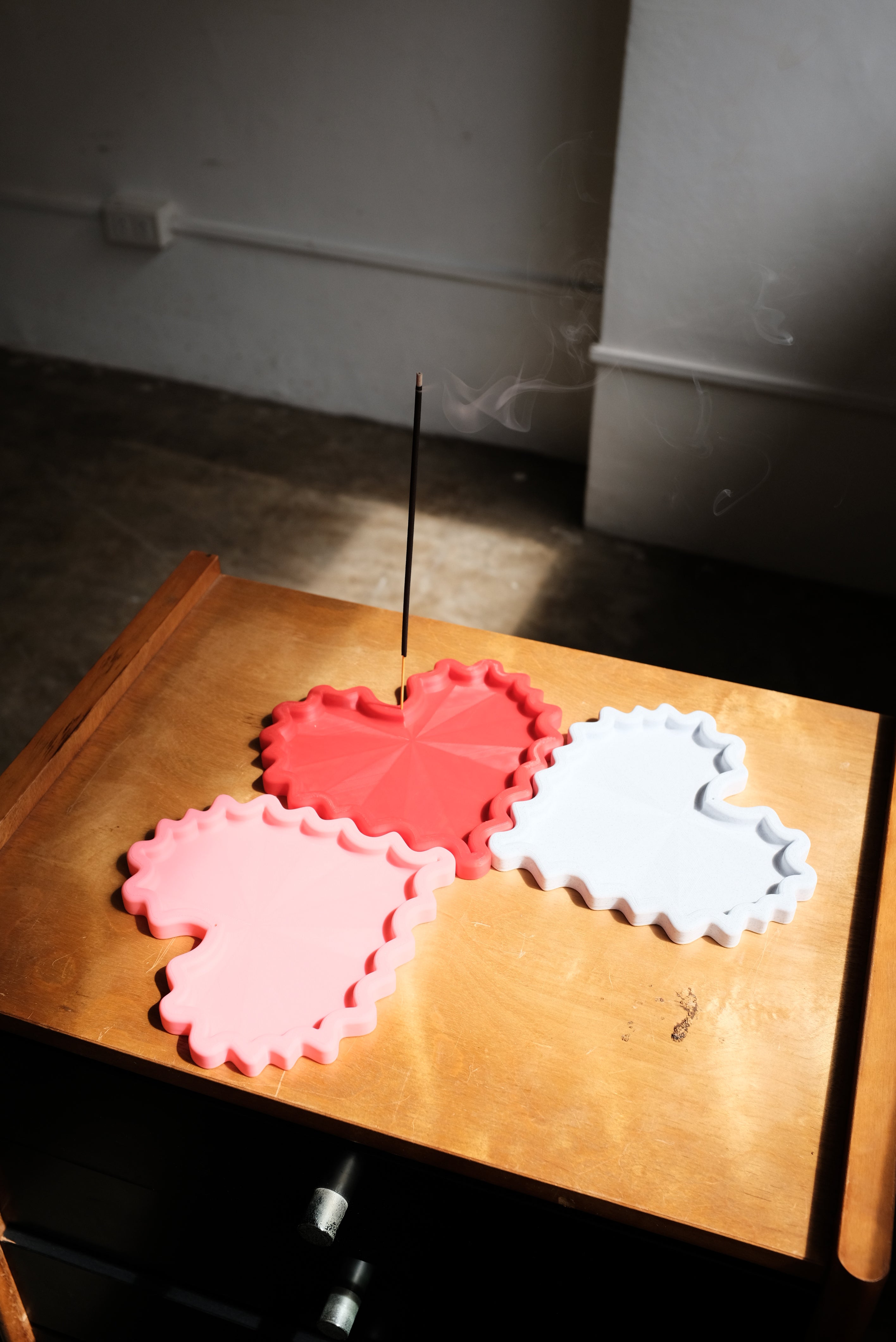 Red, pink, and white 3D printed trinket trays with an incense stick in the middle