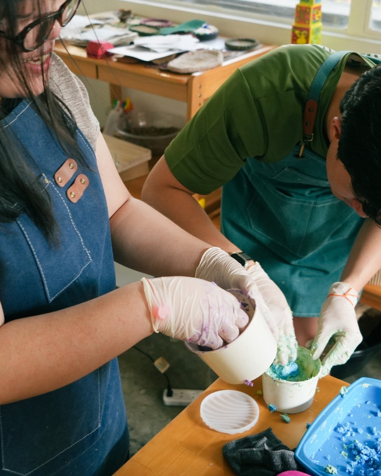 Two people in aprons and gloves working with paper pulp on a table.