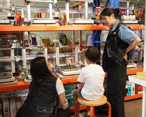 Two adults and a child in a workshop setting with shelves of equipment.