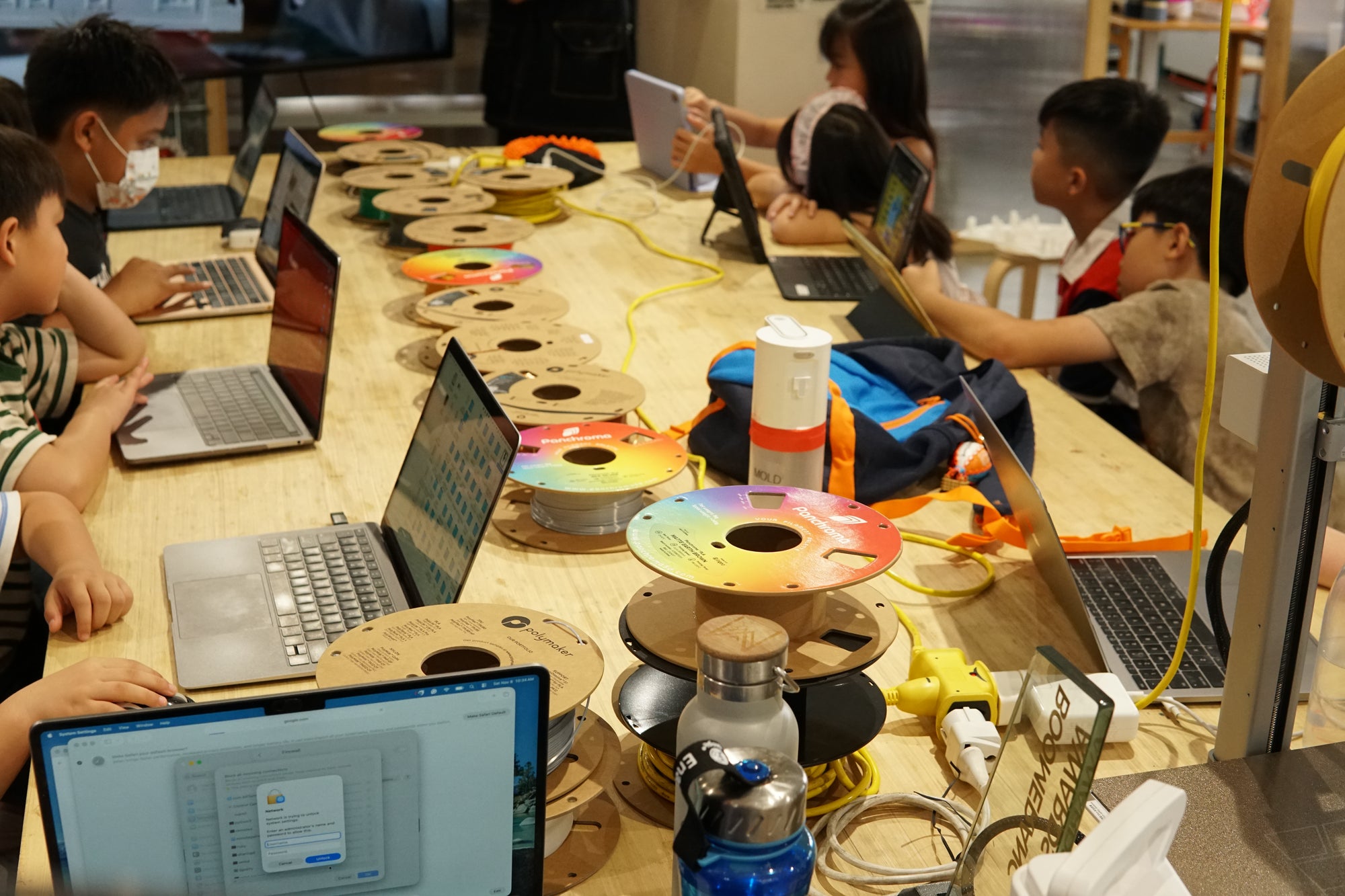 Children working on laptops at a table with electronic components